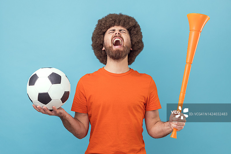 男子拿着喇叭和球，尖叫着庆祝最喜欢的足球队获胜。图片素材