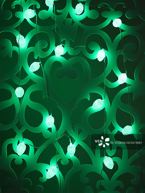 绿色冷杉球果圣诞灯花环在黑暗的背景。圣诞节或新年的彩灯花环。迷离的绿色发光灯泡花环，家居装饰。特写镜头。垂直的照片。有选择性的重点。图片素材