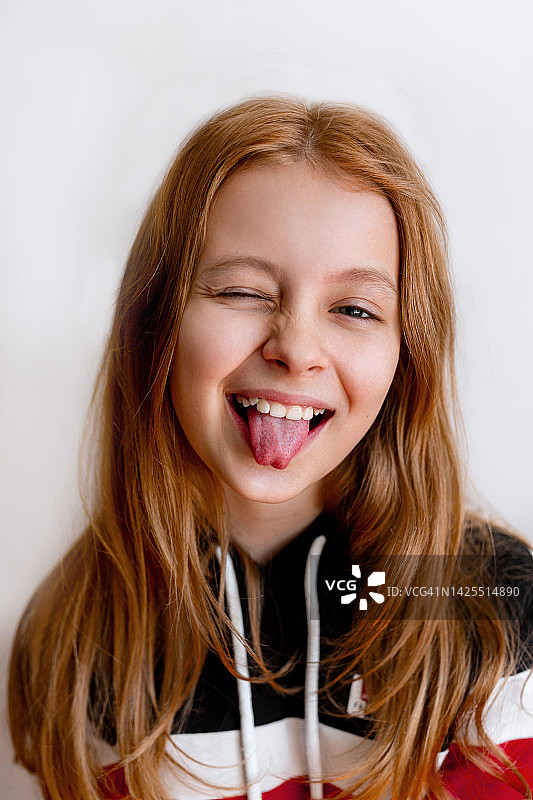 有趣的十几岁的小女孩的肖像，微笑着，在镜头里露出舌头。孩子特写肖像图片素材