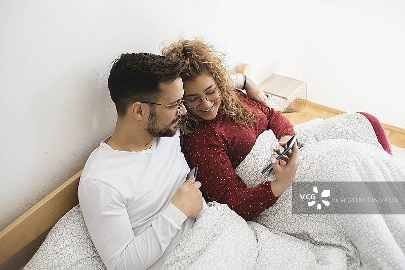 一对中年夫妇在床上使用智能手机和上网的画像图片素材