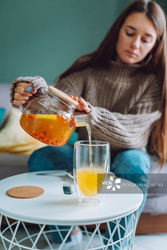 秋天暖起来了。女人的手把沙棘茶加柠檬倒进杯子里图片素材