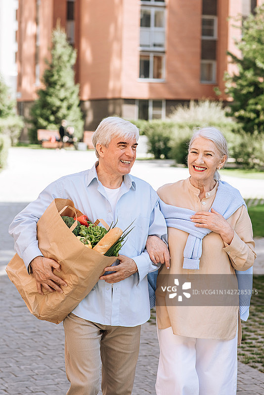 幸福的老夫妇，男人和女人一起笑着从杂货店走出来。老年人的城市生活概念图片素材