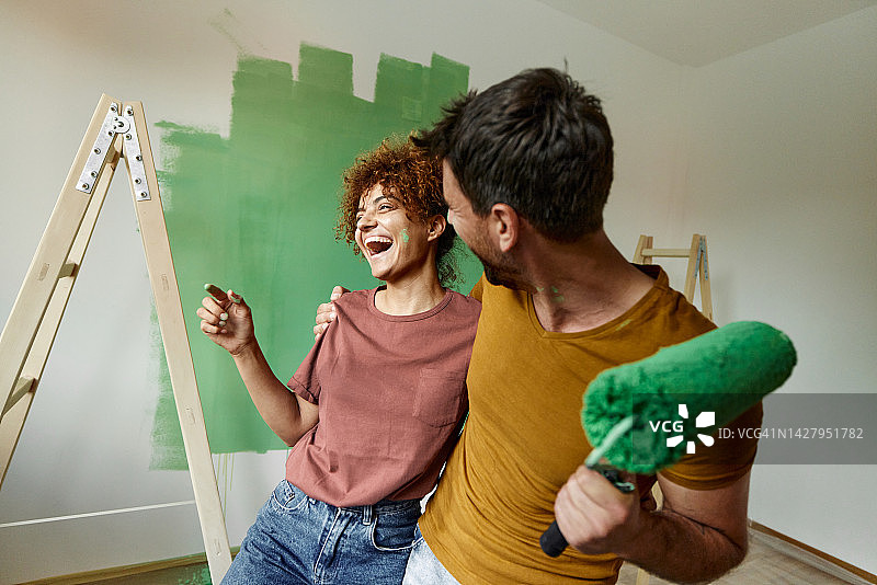快乐的夫妇在粉刷新家时拥抱在一起。图片素材