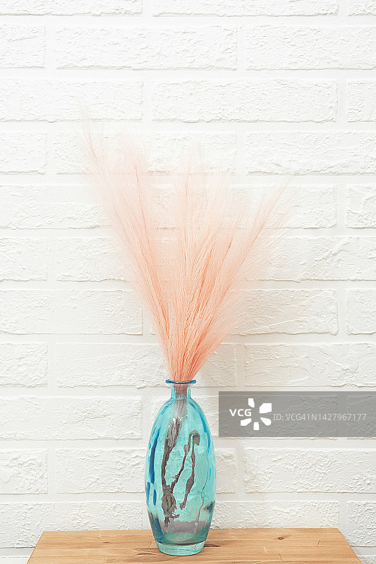 粉色潘帕斯草插在蓝色花瓶里，放在桌子上，靠白砖墙。斯堪的纳维亚设计。柔和中性色调的极简构图。图片素材