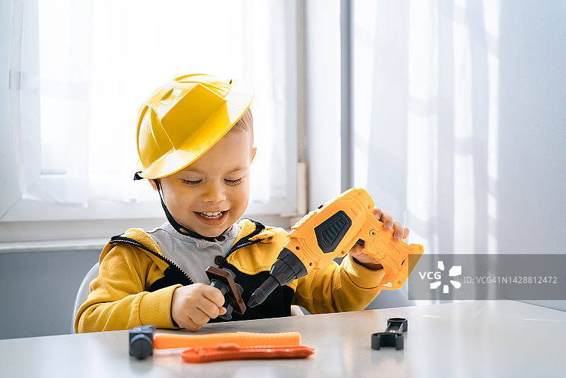 孩子在家里玩工作工具，梦想成为工程师。小男孩建设者。教育，想象力，目的性概念。孩子和钻图片素材