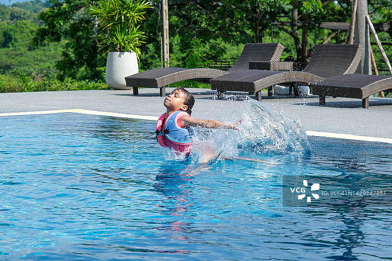 暑假期间，小女孩在热带度假胜地的室外游泳池玩耍。孩子们正在学习游泳。孩子们的健康夏季活动。图片素材