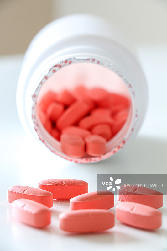 垂直拍摄的红色药片胶囊药片溢出瓶子，保健和医药的概念图片素材