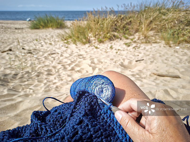 在海滩上编织蓝色围巾的女人。图片素材