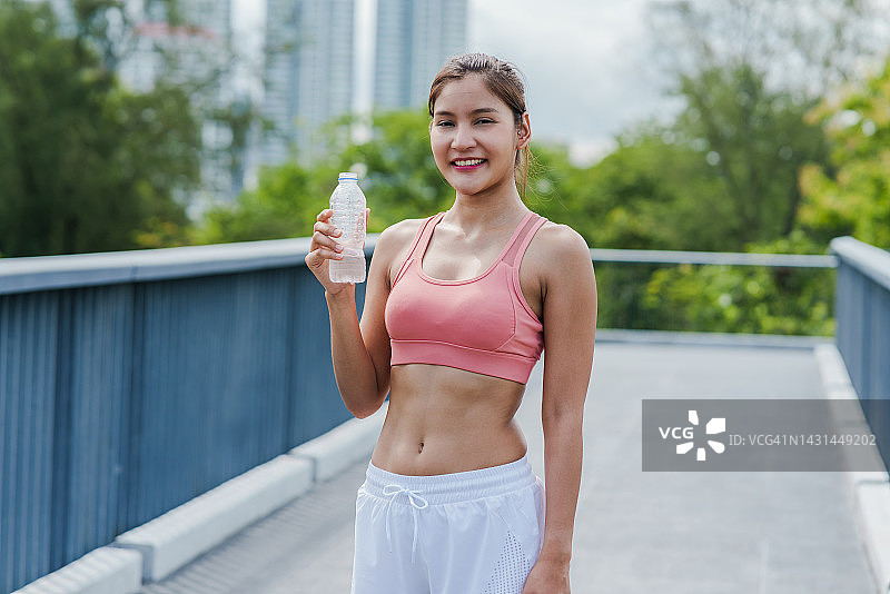 迷人的年轻运动妇女在公园里锻炼时拿着一瓶水图片素材