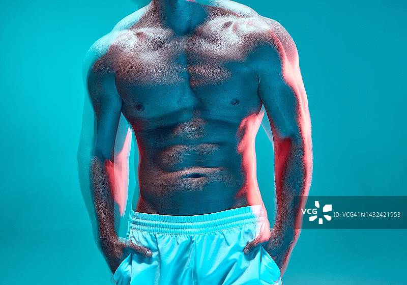 男性躯干肌肉。运动赤膊男子训练胸部和腹部肌肉在蓝色背景。长时间曝光图片素材