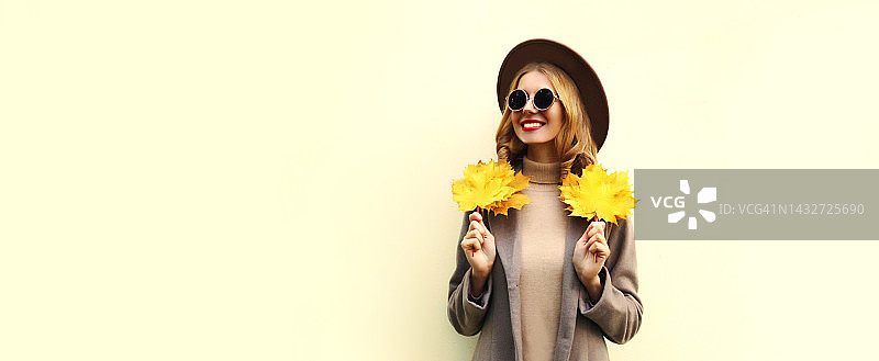 秋天的画像，美丽的微笑的年轻女子与黄色枫叶戴圆帽，白色背景的外套图片素材