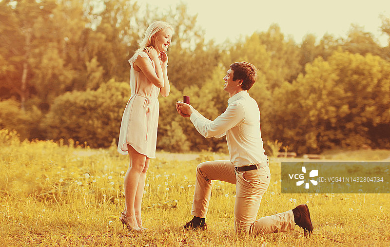 一对幸福的年轻夫妇，男人在公园里跪下来，向他心爱的女人求婚，婚礼的概念图片素材