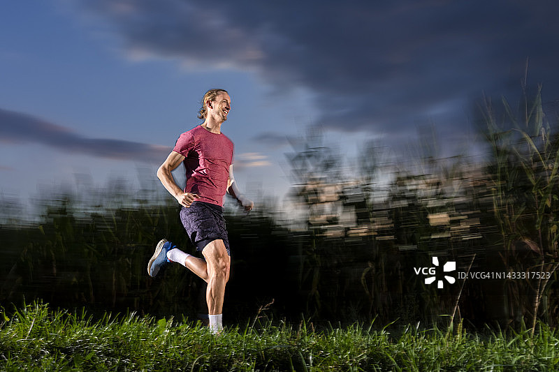 微笑的运动员在黄昏的草地上奔跑图片素材