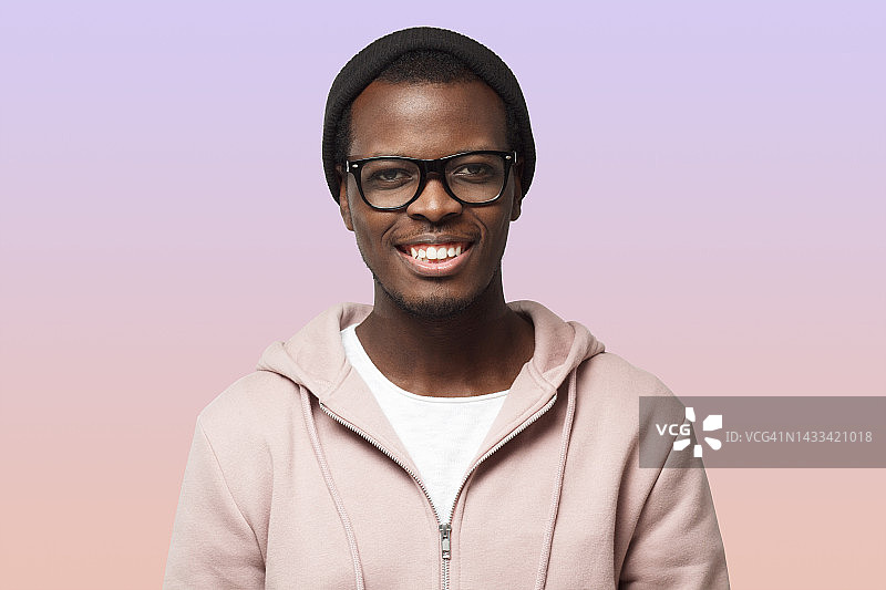 特写肖像微笑的黑人男子在粉红色卫衣，孤立的紫色背景图片素材