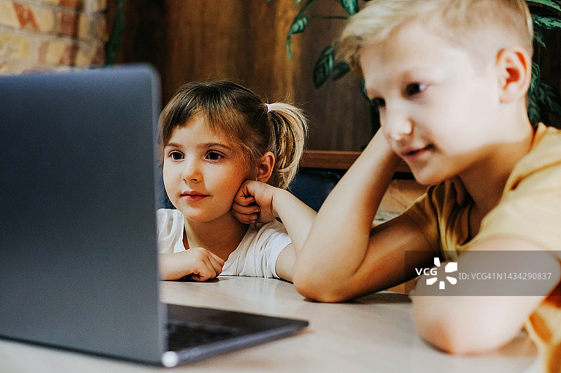 在线学习。孩子们坐在桌子旁，看着笔记本电脑的屏幕。哥哥和姐姐一起学习图片素材