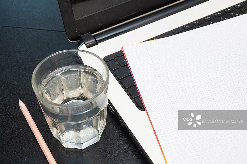 笔记本电脑键盘上的笔记本电脑旁边有一杯水。图片素材