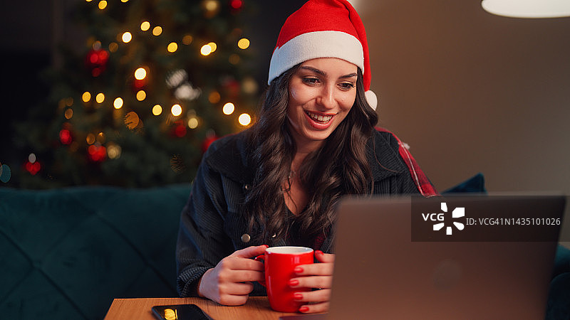 圣诞节期间，年轻女子在家里的客厅里享受着使用笔记本电脑和视频通话的乐趣图片素材