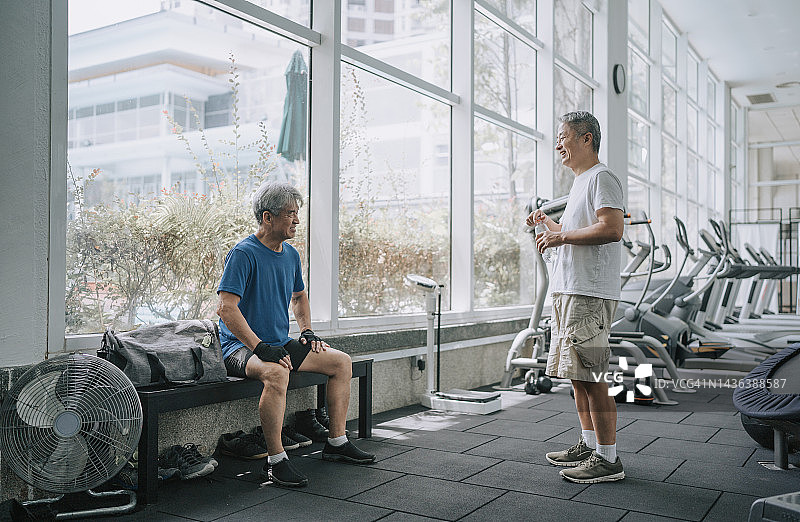 两名亚洲华裔老年男子在健身房里休息，锻炼后聊天图片素材