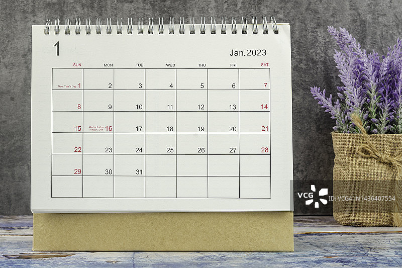 日历桌2023:一月是组织者计划和截止日期的月份，在水泥墙背景的木桌上手工制作了一朵花。图片素材