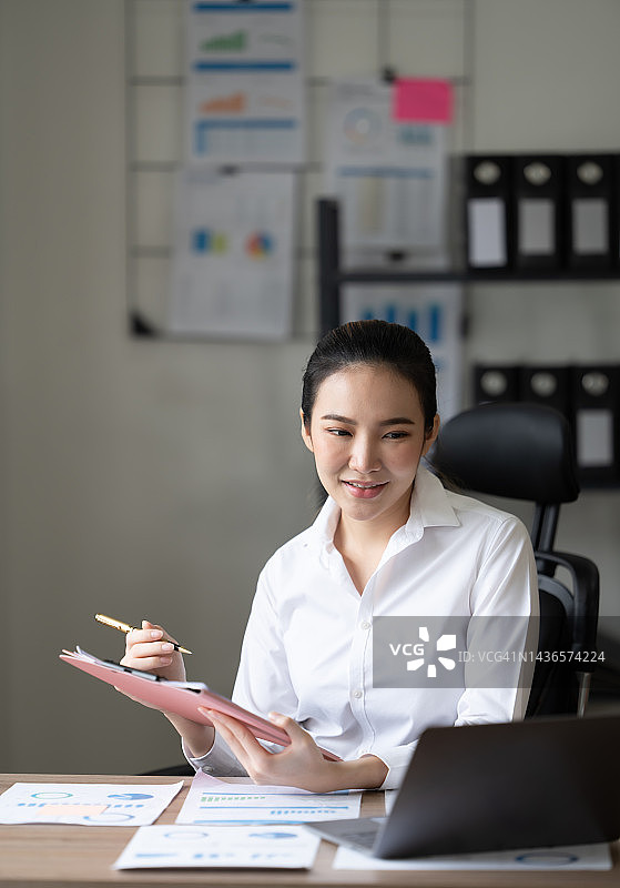 可爱的亚洲女人一边喝茶一边在办公室使用笔记本电脑图片素材