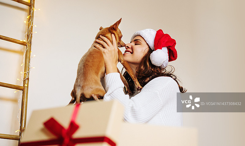 戴着圣诞帽的女人手里拿着圣诞礼物的小狗。图片素材