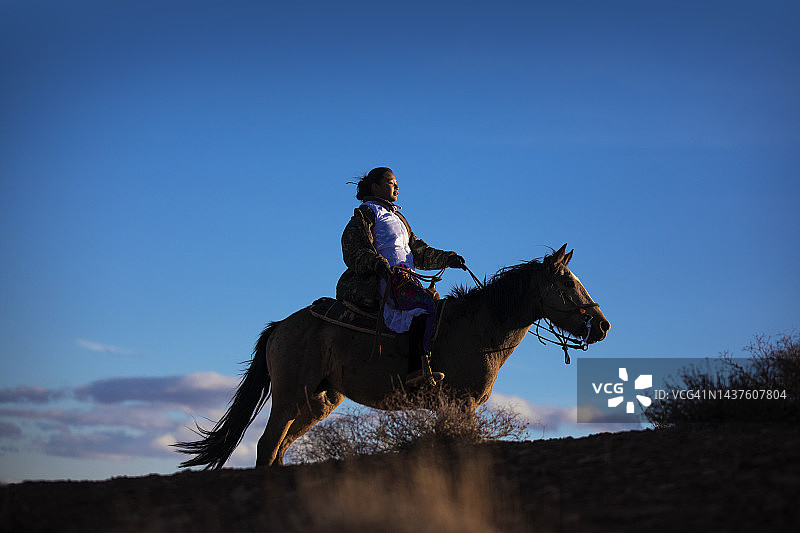 年轻的纳瓦霍女孩骑着马在日落时分的亚利桑那沙漠里快速奔跑图片素材
