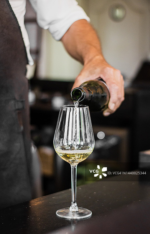 一个调酒师用模糊的背景把酒倒进玻璃杯的垂直镜头图片素材