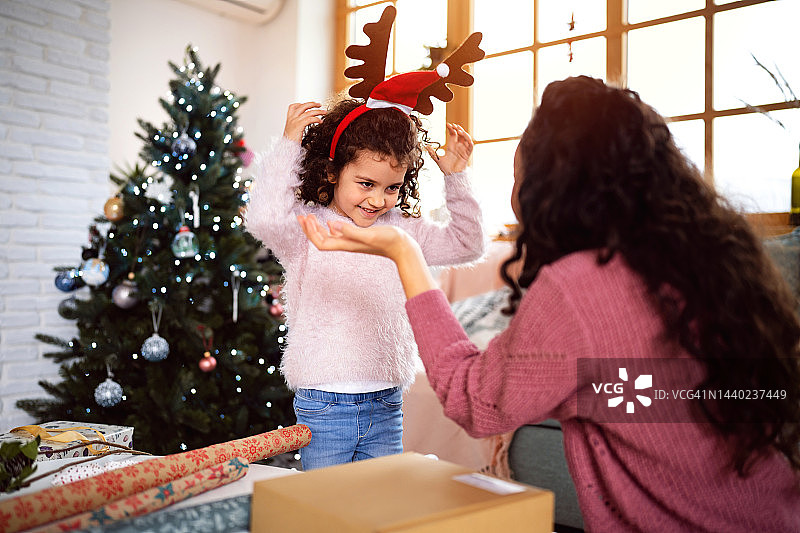 小女孩戴着驯鹿鹿角，和妈妈一起包装圣诞礼物图片素材