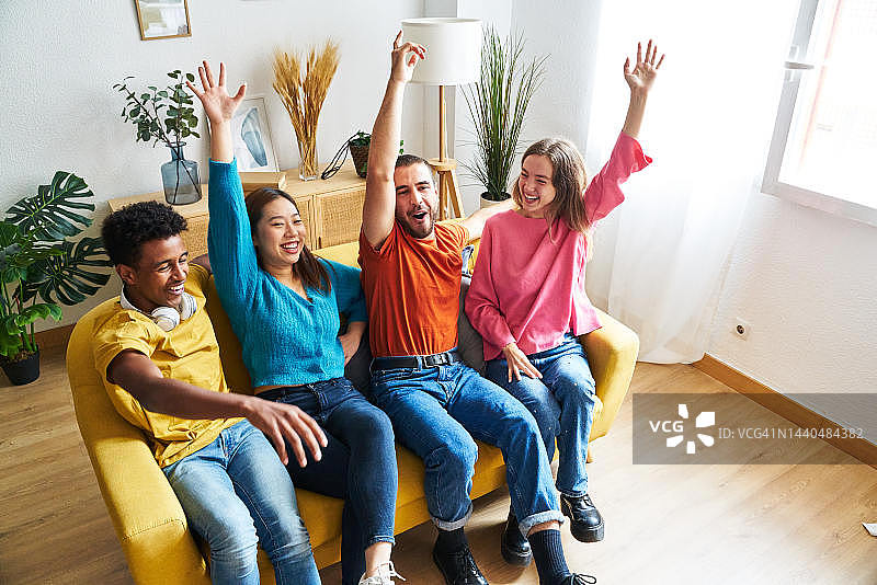 四个朋友坐在客厅沙发上看足球比赛，庆祝他们球队的进球。图片素材