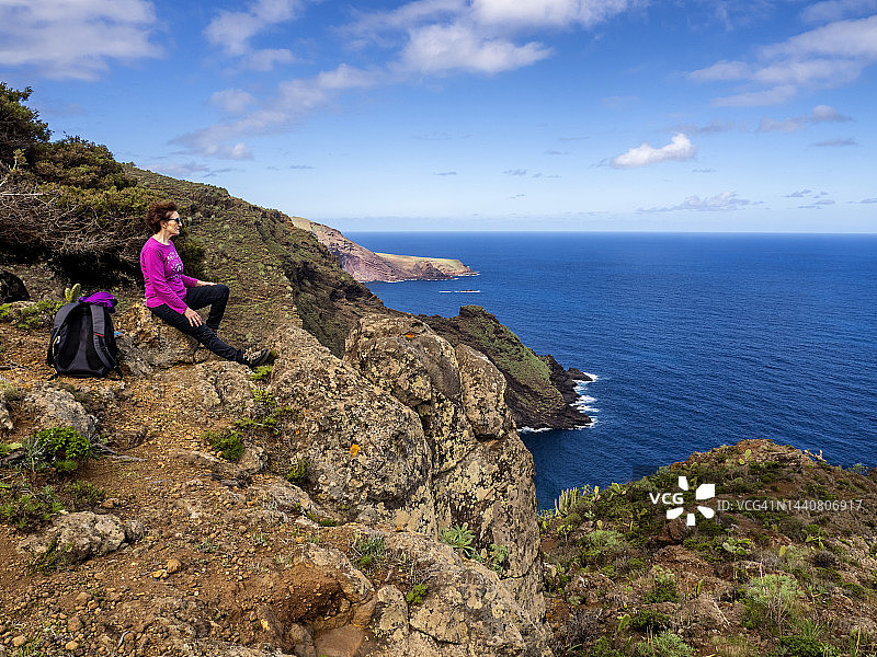 在加那利群岛，女人坐着休息，沉思着海边的悬崖景观。图片素材
