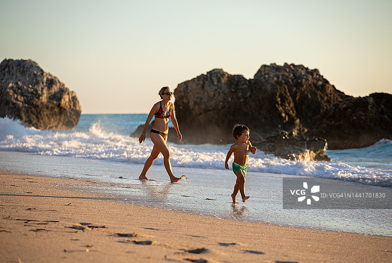 小男孩和他的母亲走在海岸线的沙滩上图片素材