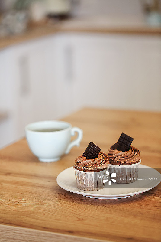 两个松饼放在白色的盘子里，点缀着可可奶油和巧克力，一杯茶图片素材