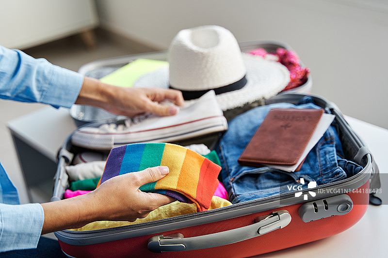 面目全非的女子把彩虹色的袜子放在行李箱里，里面装着旅行用的衣服和配件。图片素材