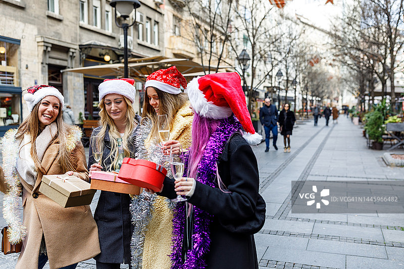 一群戴着圣诞帽的女性朋友在城市街道上度假。图片素材