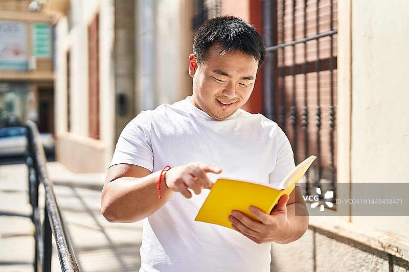 年轻的中国男子微笑着自信地在街上看书图片素材