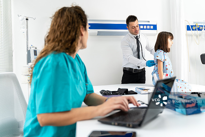 女护士长和专业医生为小女孩病人做检查。他们聊天，检查电脑的重要信息图片素材