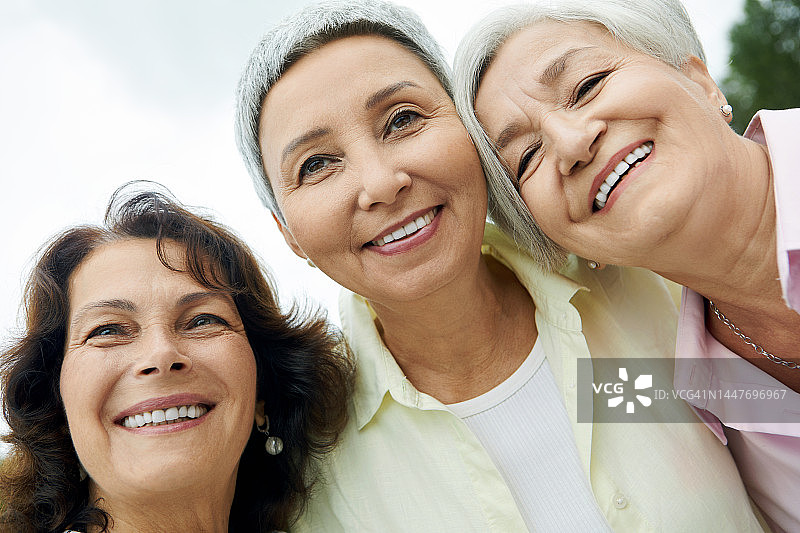 三个快乐的老妇人微笑着盯着相机，拉近肖像图片素材