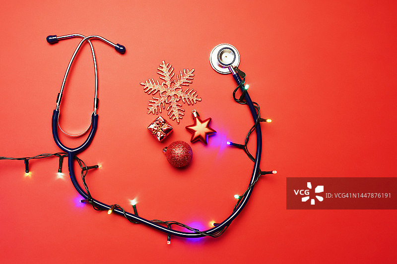 快乐健康的新年装饰。听诊器、圣诞彩灯和红色背景的圣诞装饰品图片素材