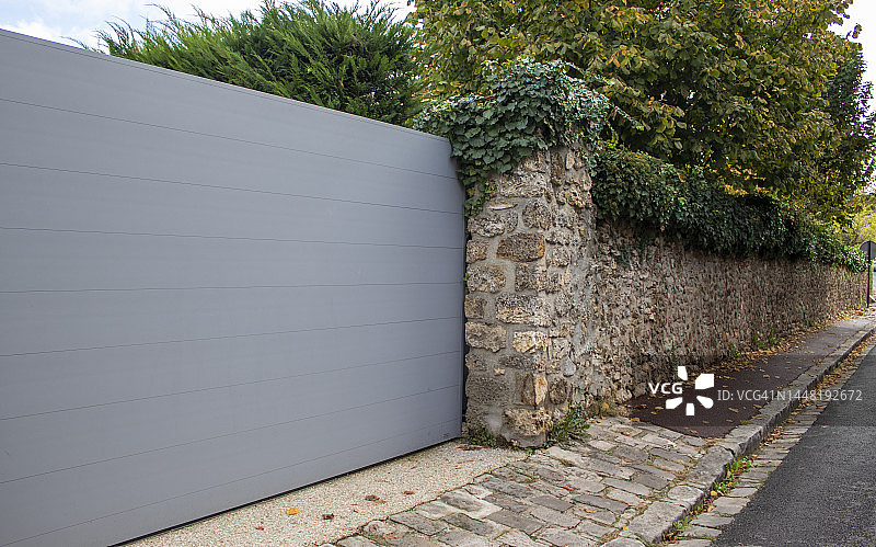 铝滑动现代灰色门户设计郊区滑动住宅花园门。在法国巴黎，通往一所房子的带金属门的石头栅栏。图片素材
