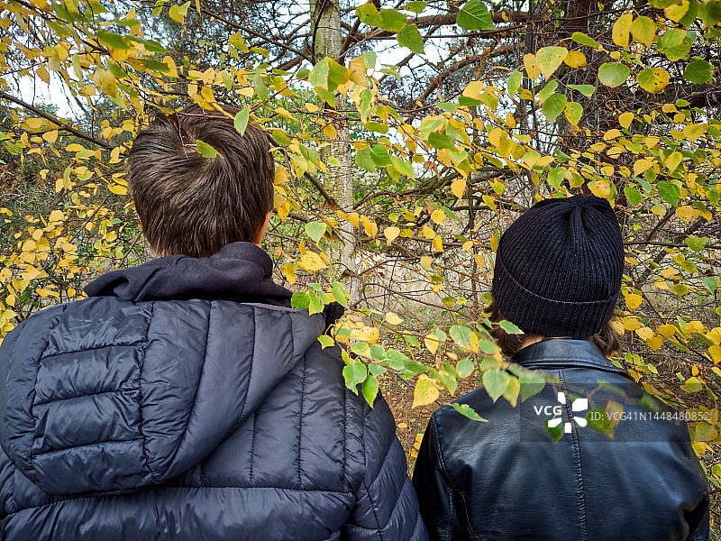 一个十几岁的男孩和女孩站在树叶之间的后视图。图片素材