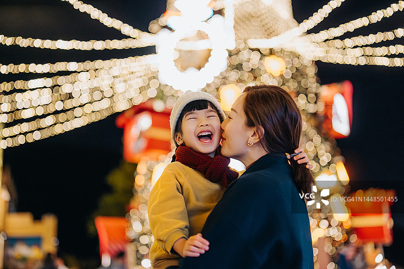 一位可爱的年轻亚洲母亲在圣诞树前抱着女儿亲吻女儿。分享快乐时刻，开心微笑。家庭生活方式。享受圣诞节的气氛。节日气氛。圣诞节到了图片素材