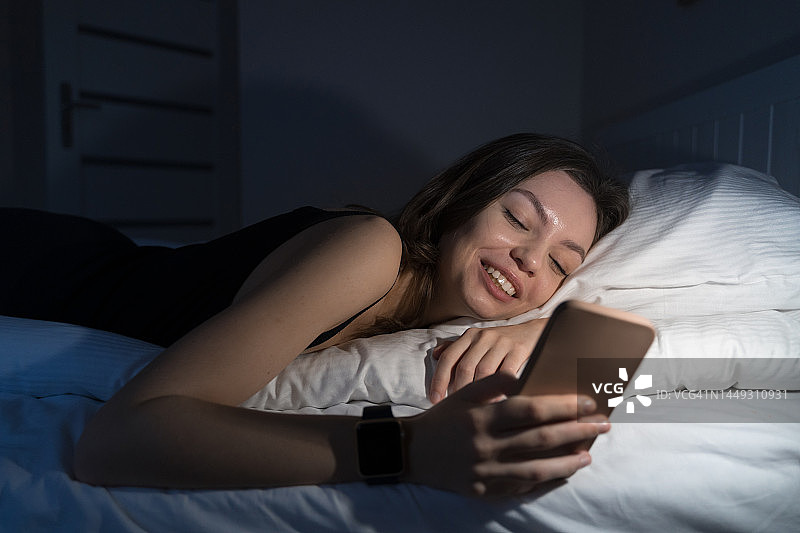 年轻女子在床上使用手机，失眠概念图片素材