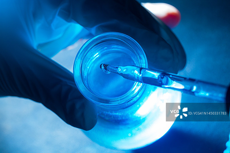 蓝色科学试管，科学家手中的烧瓶与试管中的化学液体滴科学和医学研发概念。图片素材