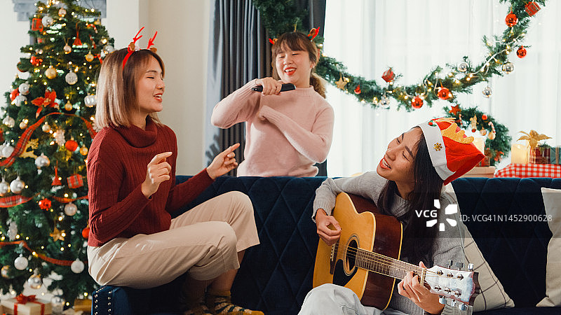 一群年轻的亚洲朋友在家里客厅的沙发上用电视控制器唱歌和弹吉他。图片素材