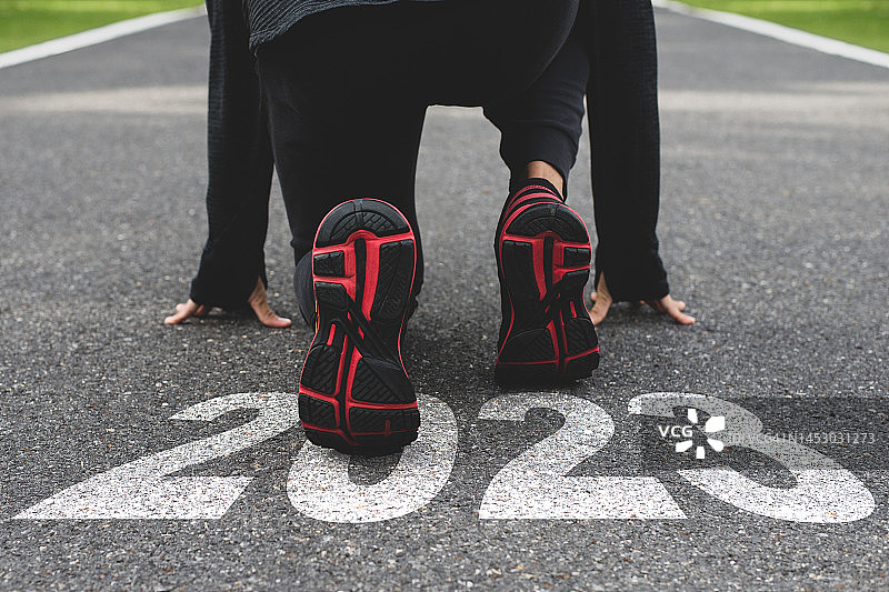 一个穿着运动服和运动鞋的年轻人准备在刻有2023年的田径跑道上出发。图片素材