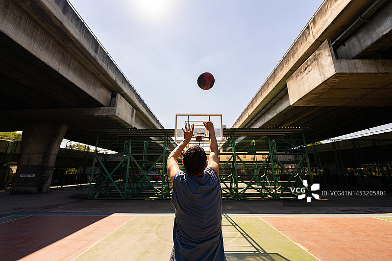 亚洲运动员在阳光明媚的户外场地练习投篮。图片素材