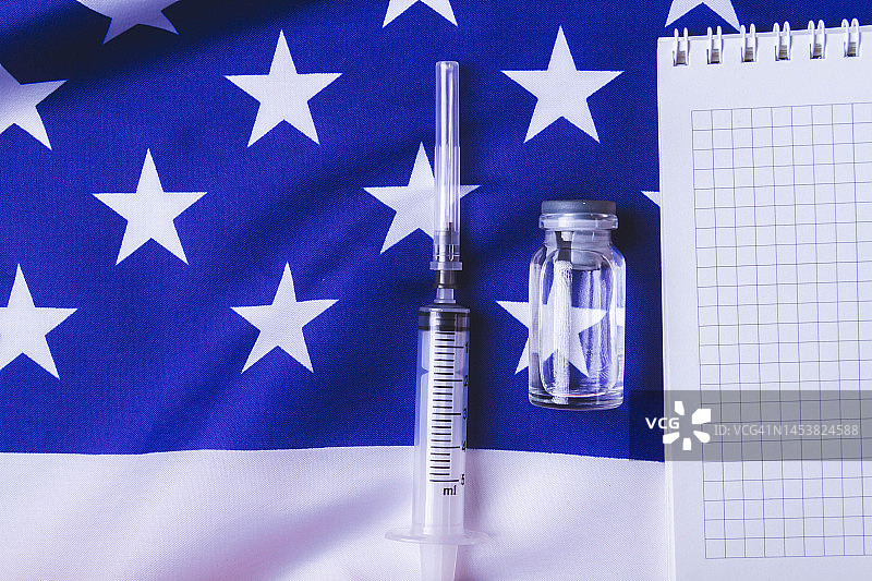 注射器和疫苗的背景是美国国旗。在萨沙接种疫苗。空白记事本用于接种疫苗记录。图片素材