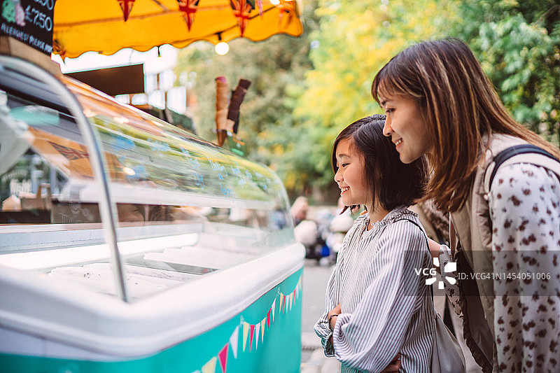 可爱的女孩和她年轻的妈妈在快餐车上买冰淇淋图片素材