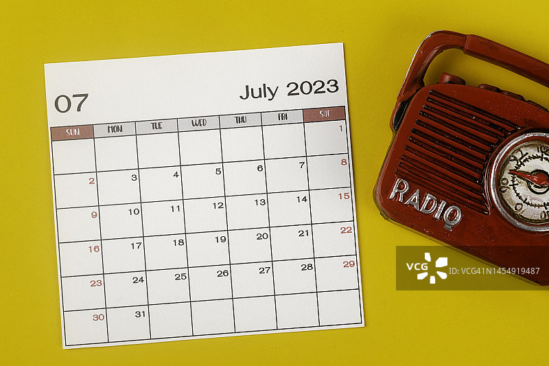 2023日历台:7月是组织者计划和截止日期的月份，背景是黄色的老式收音机。图片素材