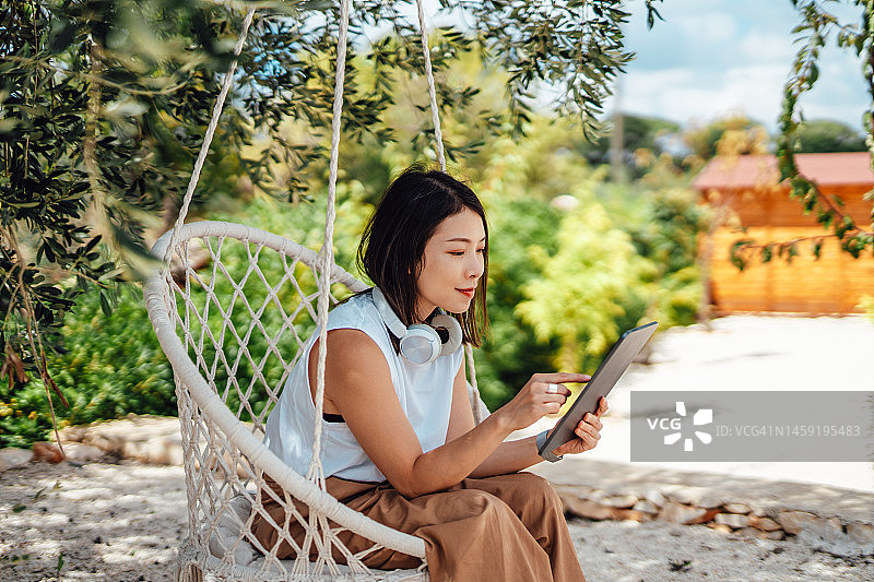 年轻的亚洲妇女工作与数字平板电脑在家里的花园放松图片素材